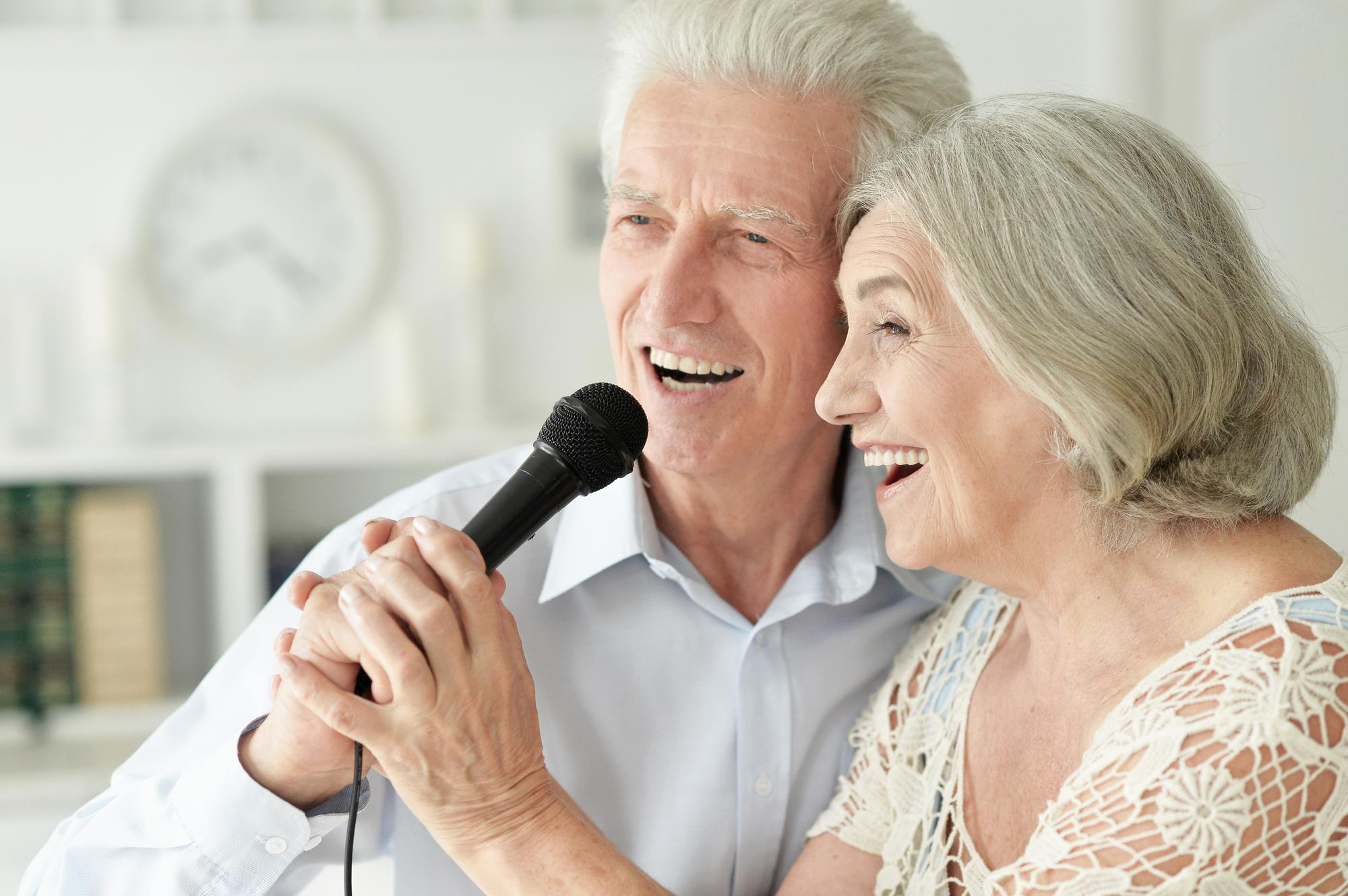 An older couple smiling and singing together, a moment of joy in a care home setting.